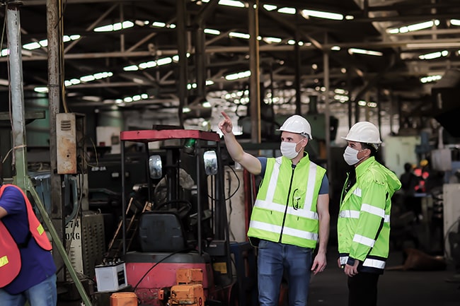 Men in green safety vests and construction hats in manufacturing plant supervising industrial equipment installation services